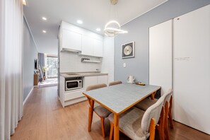 Una cocina moderna con armarios blancos, microondas integrado y comedor con mesa gris y sillas de madera.