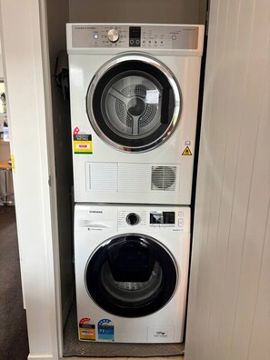 A stacked washer and dryer unit with energy efficiency labels and safety warnings.