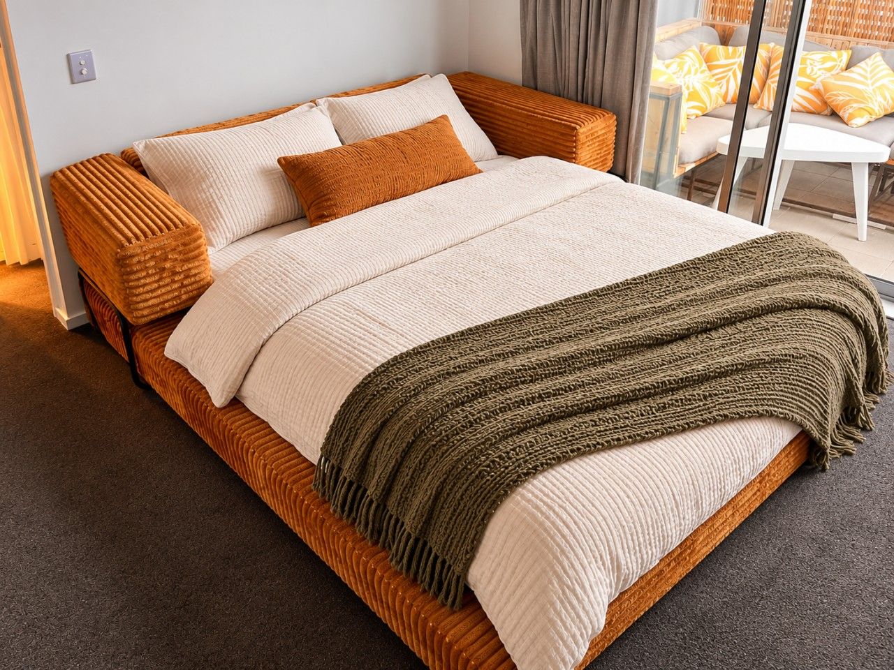 Una cama con estructura de madera, ropa de cama blanca y una manta verde.