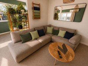 Ein Wohnzimmer mit Ecksofa, rundem Couchtisch und einem wandmontierten Spiegel.
