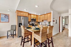 A modern kitchen with a central island, wooden cabinets, stainless steel appliances, and a dining area with wicker chairs. - Serene 1BR only 8 Min Walk to Napili Bay (Napili)