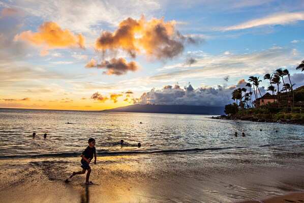 A beach scene with a sunset, palm trees, and a person running. - Serene 1BR only 8 Min Walk to Napili Bay (Napili)