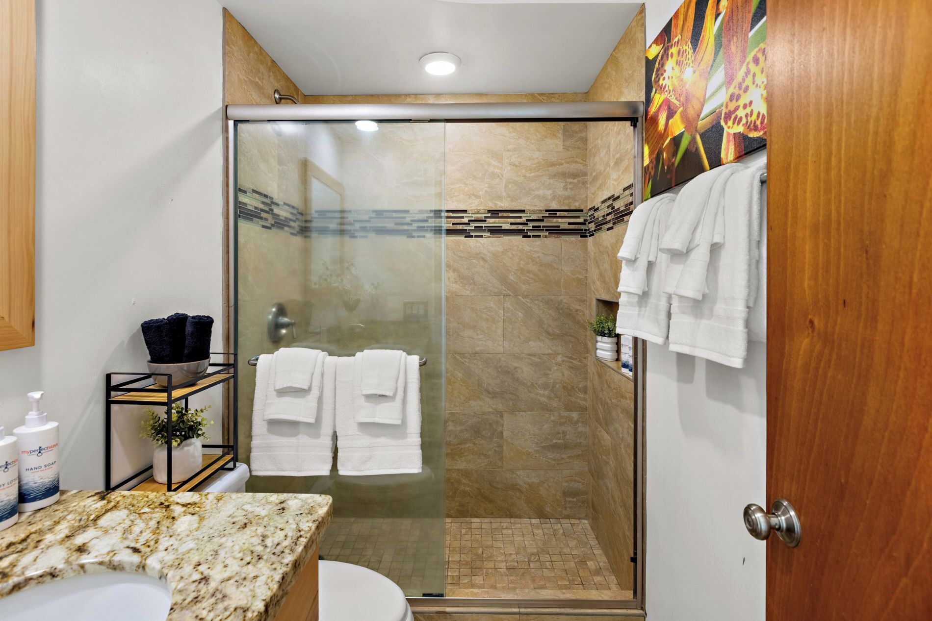 A modern bathroom with a glass-enclosed shower, marble countertops, and a wooden door.