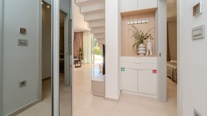 Een moderne hotellobby met een glazen deur naar een zithoek, een receptiebalie en een plant aan de muur.