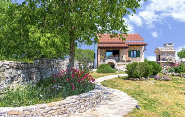 Ein Haus aus Stein mit rotem Ziegeldach, einem Steinweg und einem Garten mit Blumen und Sträuchern.