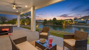 An outdoor patio with wicker furniture, a hot tub, and a view of a lake at dusk. - Waterfront Fun, Fishing & Hot Tub Retreat for Families and Friends - Blue Heron Cottage - Roelens (Cape Coral)
