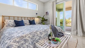 A bedroom with a large bed, a nightstand with a bottle of champagne, and a view of the outdoors. - Waterfront Fun, Fishing & Hot Tub Retreat for Families and Friends - Blue Heron Cottage - Roelens (Cape Coral)