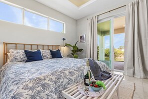 A bedroom with a large bed, a nightstand with a bottle of champagne, and a view of the outdoors. - Waterfront Fun, Fishing & Hot Tub Retreat for Families and Friends - Blue Heron Cottage - Roelens (Cape Coral)