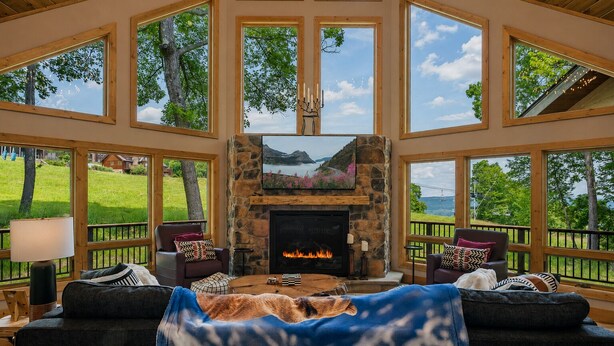 A spacious room with a stone fireplace, large windows, and a view of the outdoors. - Designer Home: Hot Tub Sauna Game Room EV Charger (McHenry)