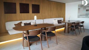 Ein modernes Wohnzimmer mit einem Holzesstisch, vier Stühlen, einem weißen Sofa mit Kissen und einer Wandlampe.