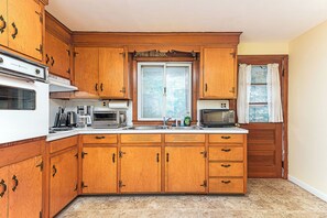Una cocina con armarios de madera, horno empotrado, microondas y una ventana con cortinas.