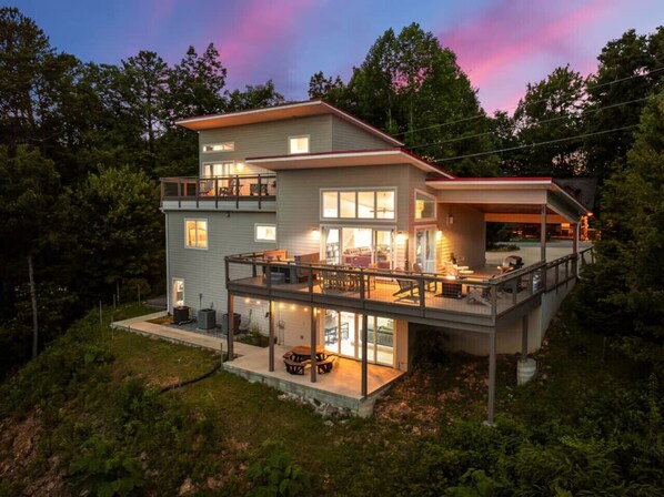 Ein modernes, zweistöckiges Haus mit Balkon, großen Fenstern und einer Terrassenfläche.