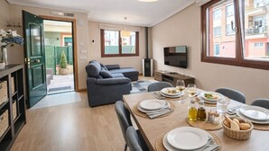 Un comedor con una mesa lista para dos personas, un sofá y un televisor al fondo.