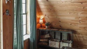 Un interior de madera con ventana, cortinas, un reloj, una lámpara y un sofá.