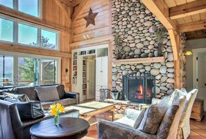 A cozy living room with a stone fireplace, leather sofas, and a large window overlooking a garden. - Three Timbers | 3 Luxury Timber Homes + Exclusive Pool Access Near Asheville (Fairview)