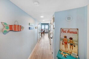 A hallway with a wooden floor, a fish decoration, and a vintage poster of children at the beach. - Sea Gull #1002: Beachfront 2 Bedroom 2 Bathroom With Spectacular Views and 24 Hour Management (Port Aransas)