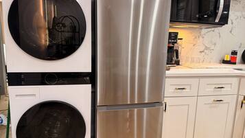 A kitchen with a stainless steel refrigerator, a washing machine, and a microwave.