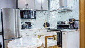 Une cuisine moderne équipée d’un réfrigérateur en acier inoxydable, d’un four à micro-ondes encastré et d’une cuisinière. On y trouve deux tabourets de bar blancs et une petite table ronde.