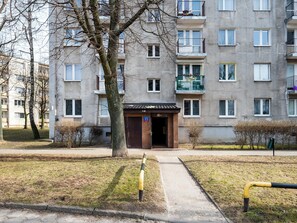 Ein mehrstöckiges Wohngebäude mit einem zentralen Eingang, einer kleinen Grünfläche und einem gepflasterten Weg zum Eingang.