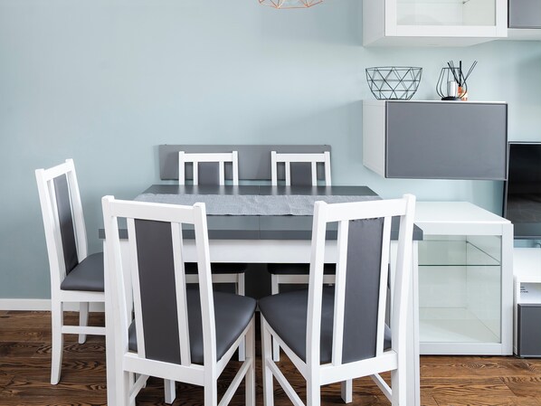 A dining area with a rectangular table, six white chairs with grey cushions, and a grey wall.