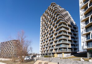 En modern höghusbyggnad med en unik, vinklad fasad, flera balkonger och en rymlig innergård.