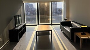 A modern living room with a sofa, a coffee table, and a TV on a stand. Large windows offer a view of the cityscape. - Work-Ready Apartment - 1 Min to Angel, CDMX (Ciudad de México)
