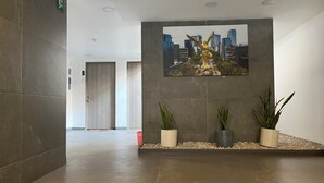 A modern hallway with a cityscape painting, potted plants, and a door at the end. - Work-Ready Apartment - 1 Min to Angel, CDMX (Ciudad de México)