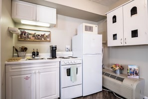 A kitchen with white cabinets, a stove, a microwave, and a refrigerator. There is a painting on the wall and a small flower arrangement on the counter. - Perfect Couple's Getaway Studio - 10 min Walk to Downtown Gatlinburg (Gatlinburg)