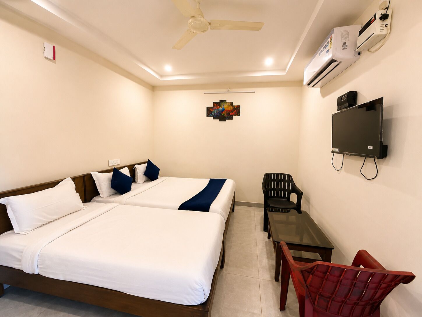 Ein Hotelzimmer mit einem Bett, einem Schreibtisch, einem Stuhl, einem Deckenventilator, einer Klimaanlage und einem Fernseher.