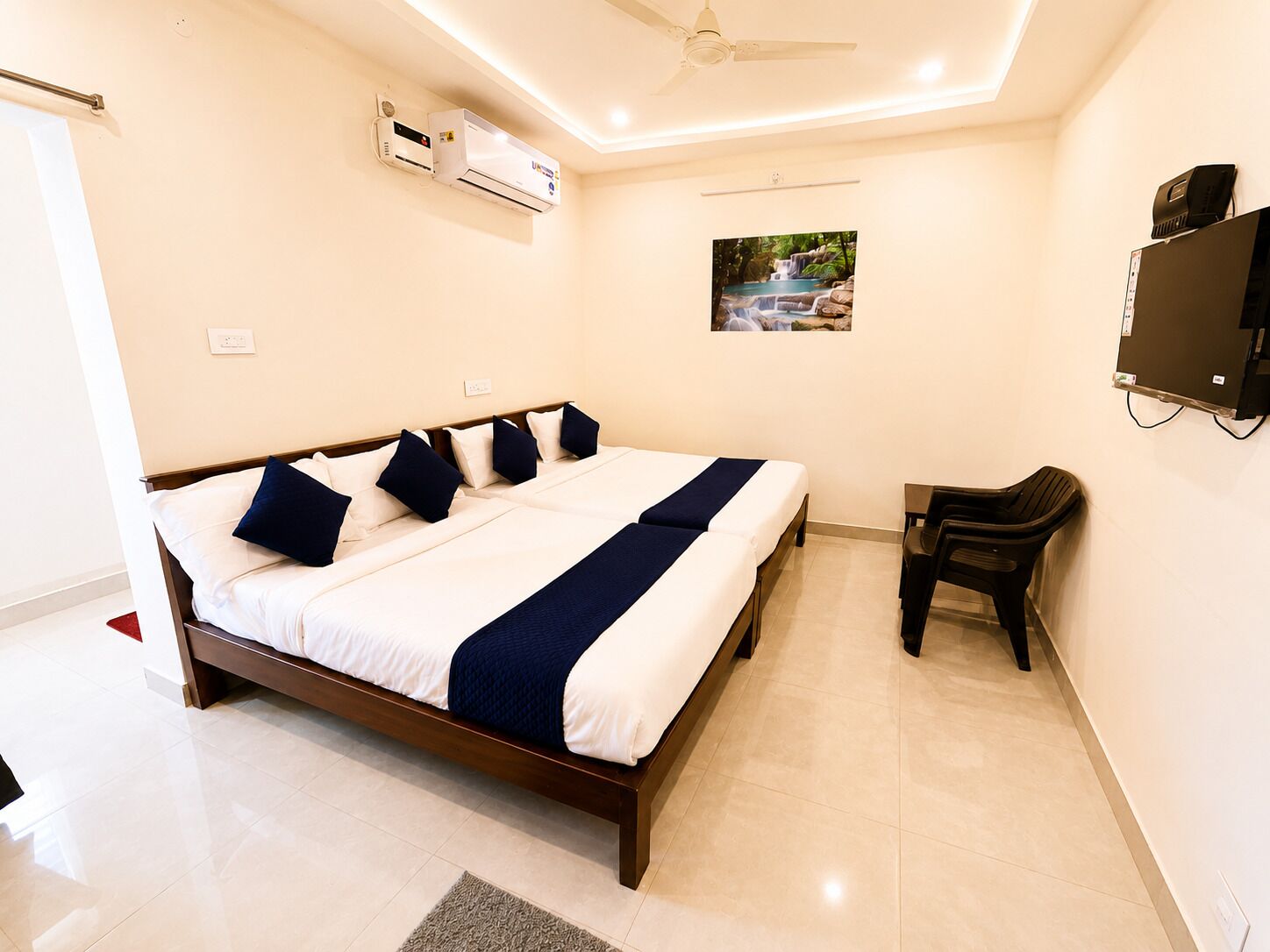 A hotel room with a bed, a desk, a chair, an air conditioning unit, a television, and a picture on the wall.