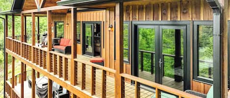 A wooden deck with outdoor seating, a covered area with a fireplace, and large sliding glass doors offering a view of the surrounding greenery.