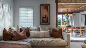 Una sala de estar acogedora con un sofá, almohadones, un cuadro y un comedor con sillas y una mesa.