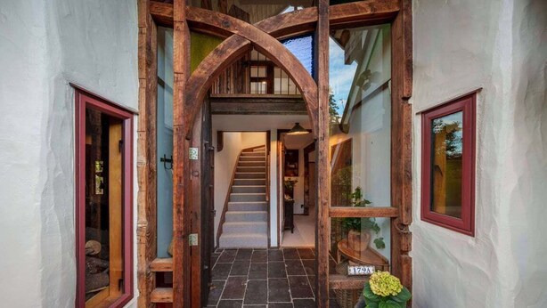 Una escalera de madera conduce a un segundo piso, con piso de baldosas de piedra y una planta en maceta en la entrada.