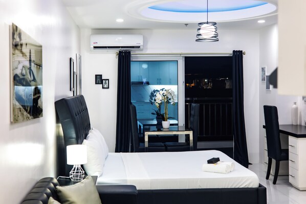 A modern hotel room with a bed, a desk, a chair, a small table with a vase, and a balcony with a view.