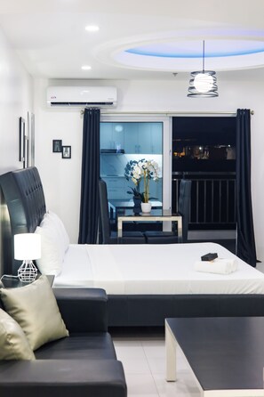 A modern hotel room with a bed, a sofa, a small table, and a view of the city at night.
