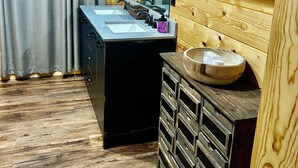 L’intérieur d’une cabane en bois, avec un évier noir, des armoires en bois et un miroir.