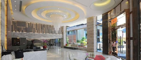 A spacious lobby with a reception desk, seating area, and large windows offering views of the outdoors.