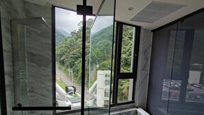 Un baño moderno con ducha envuelta en vidrio, suelo de mármol y vistas a un paisaje montañoso.