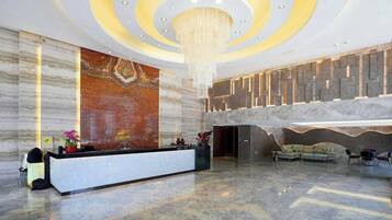 A modern lobby with a reception desk, a large abstract mural, a chandelier, and a seating area with sofas.