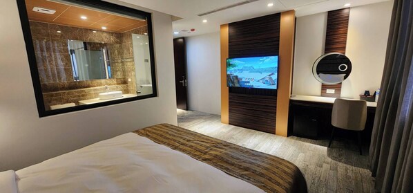 Quarto de hotel com cama, televisão, escrivaninha e banheiro.