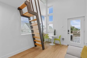 A modern interior with a wooden staircase, a dining area with two chairs and a table, and a door leading to an outdoor deck. - Seaside Pura Vida Villa steps from beach and bike path in the heart of Seaside! (Seaside)