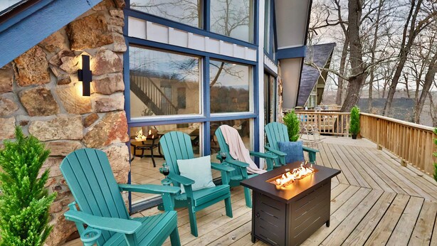 Una terraza de madera con sillas Adirondack, un pozo de fuego y un muro de piedra con amplias ventanas.
