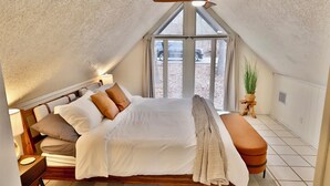 Un dormitorio con cama, un banco, un ventilador de techo y una ventana.