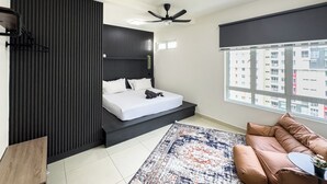 A modern bedroom with a bed, a ceiling fan, a window with a city view, and a brown leather sofa. - Residensi Suasana Damai by Airhost (Sungai Buloh)