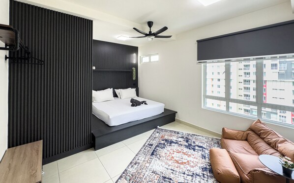 A modern bedroom with a bed, a ceiling fan, a window with a city view, and a brown leather sofa. - Residensi Suasana Damai by Airhost (Sungai Buloh)