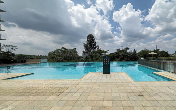 A swimming pool with tiled deck, surrounded by trees and a cloudy sky. - Residensi Suasana Damai by Airhost (Sungai Buloh)