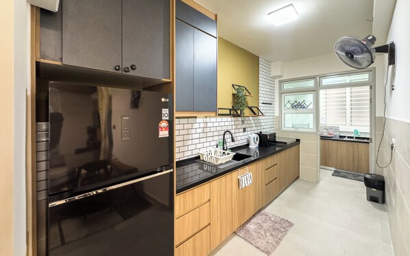 A modern kitchen with a built-in refrigerator, wooden cabinets, a black countertop, and a window with blinds. - Residensi Suasana Damai by Airhost (Sungai Buloh)