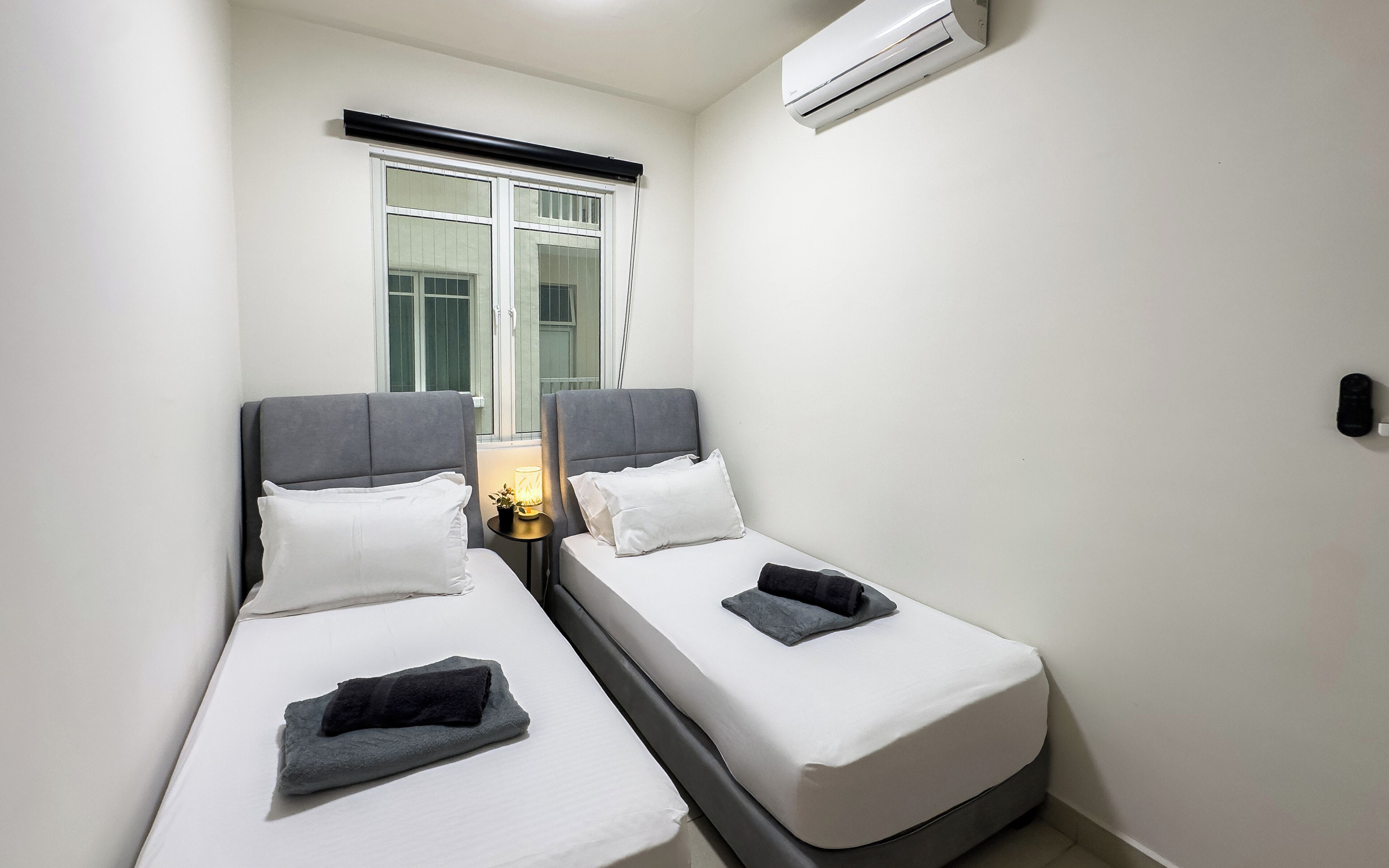 A small, clean room with two single beds, a window with a view, and an air conditioning unit.