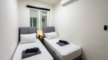 A small, clean room with two single beds, a window with a view, and an air conditioning unit.