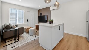 A modern kitchen with a central island, a dining area with a sofa and table, and a TV mounted on the wall. - Modern 1BR Private ADU with Dedicated Parking & Washer Dryer (Citrus Heights)